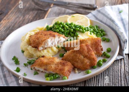 Panierter Fisch mit Kartoffelpüree und grünen Erbsen. Hausgemachtes Familienessen. Stockfoto