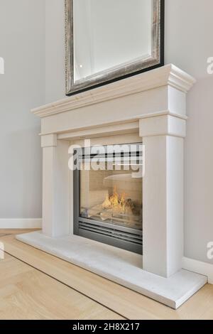 Stapel von heißem Brennholz in weißen modernen Kamin mit Schutzglas an der Wand mit Spiegel in hellen modernen Wohnung brennen Stockfoto