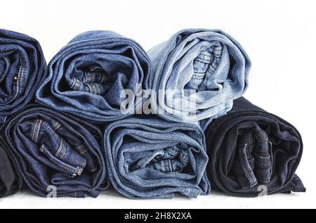 Stapel von blauen, gefalteten und zerbröckeligen Denim-Hosen, die im hellen Studio platziert sind Stockfoto