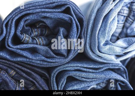 Stapel von blauen, gefalteten und zerbröckeligen Denim-Hosen, die im hellen Studio platziert sind Stockfoto