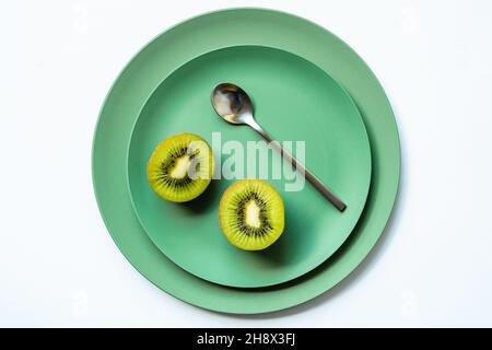 Von oben halbierte frische leckere Kiwi und silberner Löffel auf grünen Keramikplatten auf weißem Hintergrund platziert Stockfoto