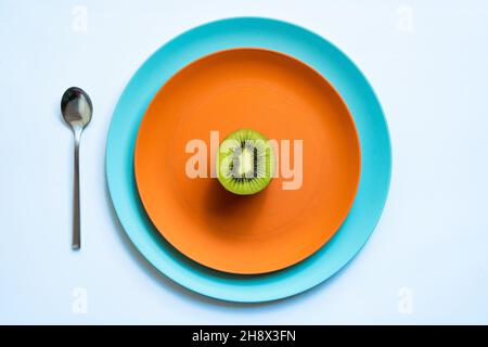 Von oben die Hälfte der frischen reifen saftigen Kiwi auf orange und blaue Teller auf weiße Oberfläche gelegt Stockfoto