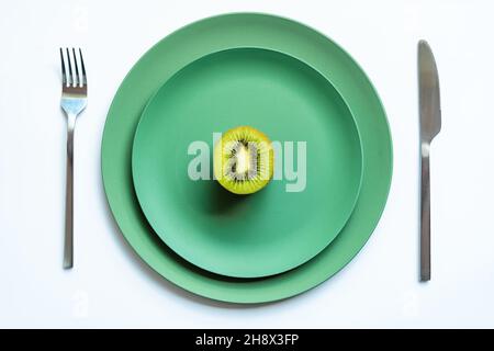 Von oben die Hälfte der frischen reifen saftigen Kiwi auf grüne Keramikplatten auf weißer Oberfläche gelegt Stockfoto