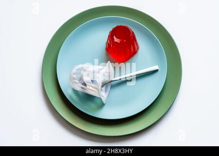 Draufsicht auf appetitliche rote Beerengelee auf hellblauen runden Teller mit Joghurtglas mit Löffel auf weißer Oberfläche gelegt Stockfoto