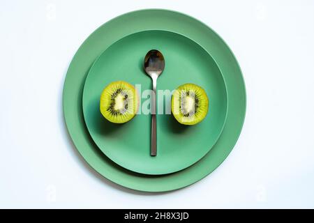 Von oben halbierte frische leckere Kiwi und silberner Löffel auf grünen Keramikplatten auf weißem Hintergrund platziert Stockfoto