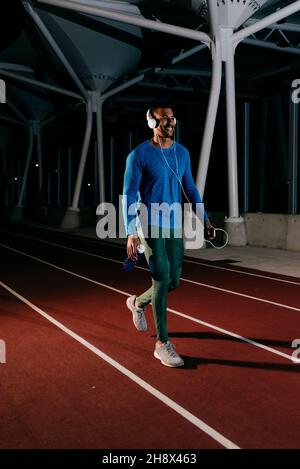 Seitenansicht eines jungen afrikanischen Athleten, der nachts Musik hört und auf der Laufstrecke läuft Stockfoto