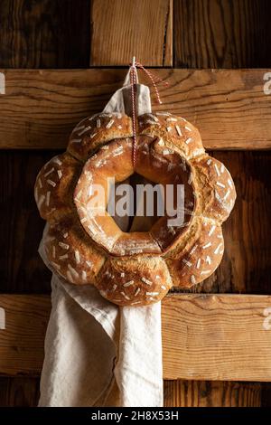 Dekorativer runder gebackener Brotlaib mit weißen Mustern, der an der Holzwand mit Handtuch in der hellen Küche zu Hause hängt Stockfoto