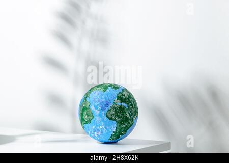 Kleiner runder Globus auf weißem Tisch im hellen Raum mit Schatten der Pflanze an der Wand bei Tageslicht Stockfoto