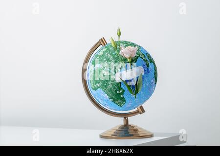 Globus des Planeten Erde mit Blumen, die mit medizinischen Hilfsband auf weißer Oberfläche angebracht sind Stockfoto