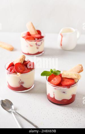 Erdbeeren-Dessert in Glasgefäßen mit Plätzchen Savoyardi, Mascarpone und Schlagsahne. Nahaufnahme. Italienische Tiramisu mit sommerlichen Vibes auf Weiß. Stockfoto