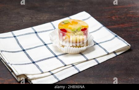 Kuchen mit Gelee, Kiwi, Kirschen und Mango auf dem Tisch. Leckeres Mini-Dessert auf einem hölzernen Hintergrund, Nahaufnahme. Stockfoto