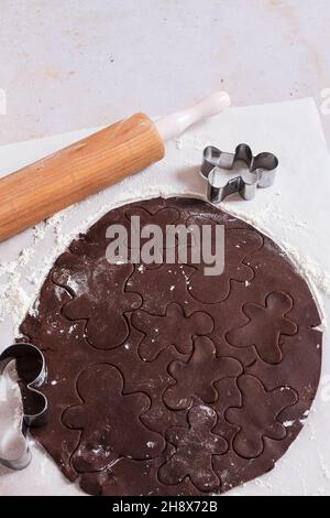 Schokoladen-Lebkuchen-Teig auf Backpapier mit ausgeschnittenen Lebkuchen Mann Formen ausgerollt. Stockfoto