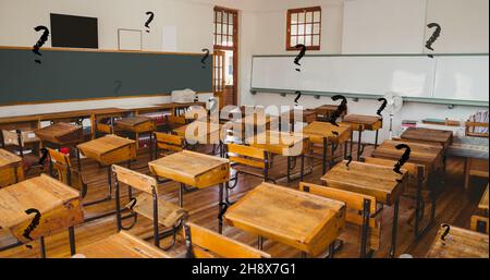 Digitale Komposition aus schwarzen Fragezeichen über leerem Klassenzimmer mit Holzschreibtischen in der Schule Stockfoto