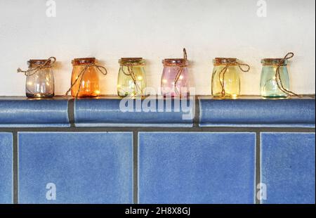 LED-Leuchten in farbigen Gläsern auf Kachelofen Stockfoto