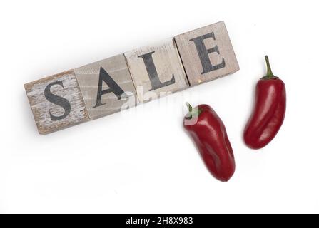 Zwei dunkelrote Paprika neben Holzwürfeln, die den Verkauf auf weißem Hintergrund als Konzept für reduzierte Preise darstellen Stockfoto