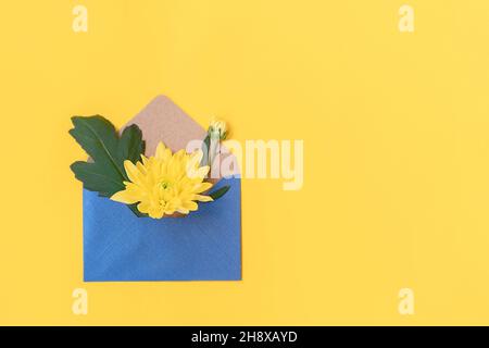 Blauer Umschlag mit Mini-Bouquet von gelben Blumen auf gelbem Hintergrund. Vorlage für Grußkarte, Einladung zur Feier. Glückliche Mütter, Frauentag, Frühlingskonzept Stockfoto