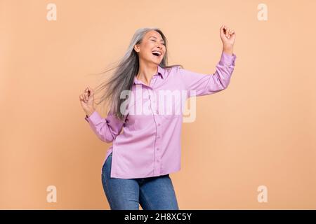 Foto von süßen grauen Frisur ältere Dame Tanz tragen violette Kleidung Jeans auf beigem Hintergrund isoliert Stockfoto