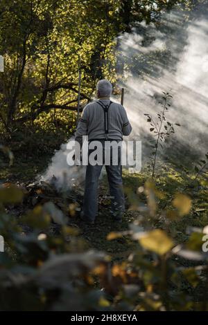 RAJHRAD, TSCHECHISCHE REPUBLIK - 22. Okt 2021: Foto eines alten Mannes, der im Herbst LaubverbrennungenEin alter Mann, der im Garten Blätter verbrennt Stockfoto