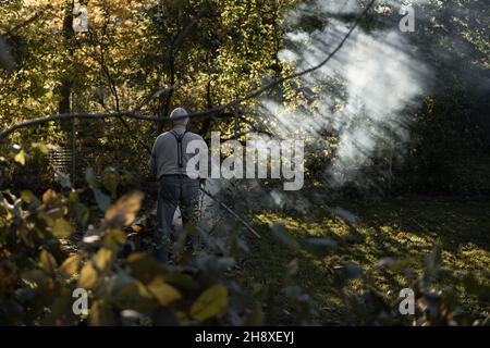 RAJHRAD, TSCHECHISCHE REPUBLIK - 22. Okt 2021: Ein alter Mann, der im Herbst Blätter im Garten verbrennt Stockfoto