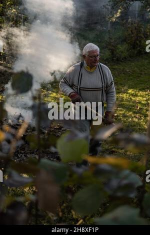 RAJHRAD, TSCHECHISCHE REPUBLIK - 22. Okt 2021: Ein alter Mann, der im Herbst Blätter im Garten verbrennt Stockfoto