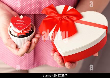 Mädchen hält herzförmigen Cupcake mit der Aufschrift Happy Valentine's Day und rote Geschenkbox. Cupcake in Form von Herz-Nahaufnahme Stockfoto