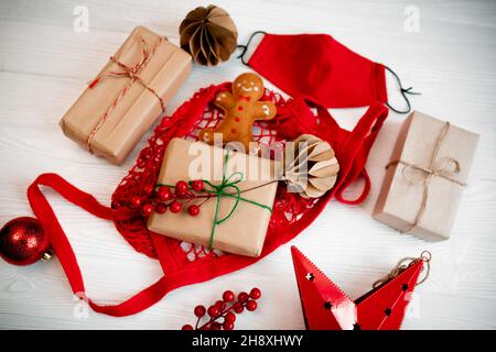 Geschenke kaufen und vor Weihnachten in Bastelpapier einwickeln. Lebkuchenmann aus Filz in einer roten Tasche mit handgefertigten Christbaumspielzeug und Gesichtsmaske Stockfoto