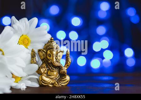 Goldener lord ganesha-Sklupture in Gänseblümchen-Blumen auf blau beleuchtetem Hintergrund. Platz für Text kopieren Stockfoto