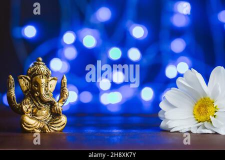 Goldener lord ganesha-Sklupture in Gänseblümchen-Blumen auf blau beleuchtetem Hintergrund. Platz für Text kopieren Stockfoto