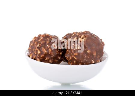 Drei süße Schokoladen-Bonbons mit Nüssen auf einer weißen Keramikuntertasse, Nahaufnahme, isoliert auf Weiß. Stockfoto