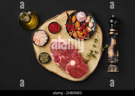 Blick von oben auf rohes, frisches Lammfleisch mit mittelgeschnittenem Bein und Gewürzen auf Holzplatte Stockfoto