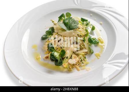 Artischockensalat mit Lammsalat, Parmesan-Flocken und nativem Olivenöl extra in weißem Teller, isoliert auf Weiß Stockfoto