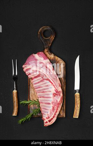 Draufsicht auf rohe, frische Lammrippen, ungeschnitten mit Gabel und Messer zum Grill Stockfoto