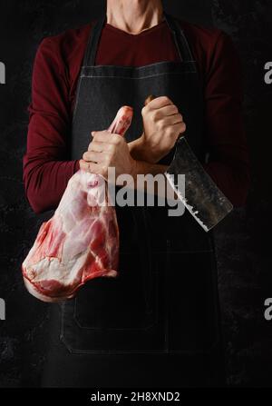 Der Metzger hält rohes Lammbein in einer Hand und das Hackfleisch in einer anderen auf dunklem Hintergrund Stockfoto