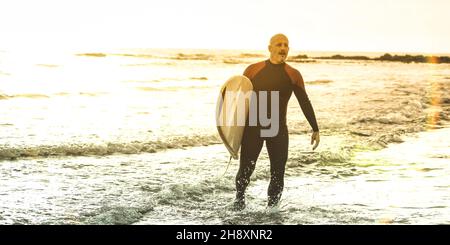 Guy Surfer Walking mit Surfboard bei Sonnenuntergang auf Teneriffa - Surf Long Board Training Practitioner in Aktion - Sportreisekonzept mit weichem Fokus Stockfoto