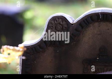 Nahaufnahme eines alten Grabsteines mit Spinnweben um ihn herum und hellem Sonnenlicht, das auf ihm auf einem Friedhof scheint Stockfoto