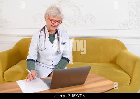 Lächelnde Ärztin im mittleren Alter von 60s Jahren, die die Kamera anschaut. Glückliche reife elegante alte Dame posiert im Krankenhaus Stockfoto