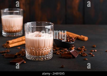 Glas irischer Rahm-Baileys-Likör mit gerösteten Kaffeebohnen, Zimt und Schokolade auf dunklem Holz-Hintergrundtisch. Selektiver Fokus. Stockfoto