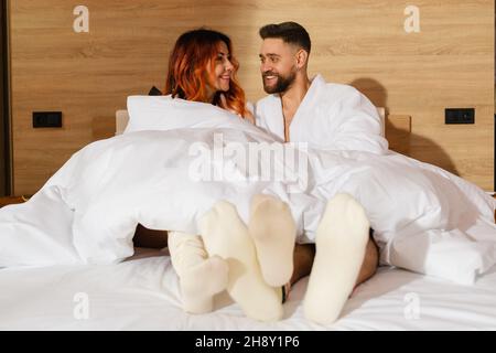 Ein junges Paar, ein Mann und eine Frau, liegen in weißen Bademänteln im Bett. Stockfoto