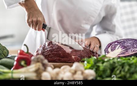 Ein Stück Schweinefleisch wurde mit einem scharfen Messer von einem professionellen Koch mit viel Gemüse geschnitten. Stockfoto