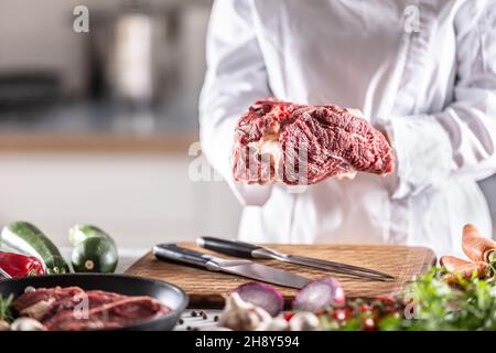 Detail eines Küchenchefs, der ein großes Stück rotes Fleisch in den Händen hält. Stockfoto