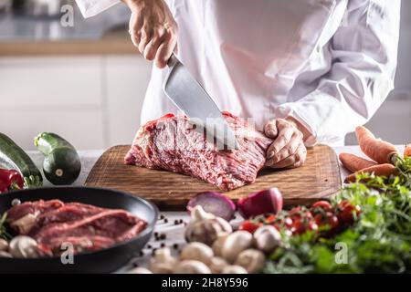 Der Küchenchef schneidet im Restaurant mit einem großen Messer ein Stück rotes Fleisch. Stockfoto