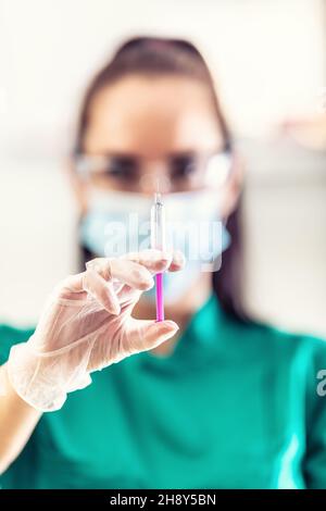 Detail einer Injektion mit einem Impfstoff, der von einem Arzt in Schutzmaske, Handschuhen und Schutzbrille getestet wurde. Stockfoto