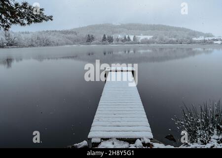 Hölzerner Pier auf See mit frischem Schnee bedeckt.Winterteich mit kleinem Steg am nebligen Morgen.Foggy bewölkte Landschaft im Wasser reflektiert. Weißer Winter Stockfoto