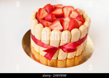 Tiramisu-Kuchen mit Erdbeeren, Marienkäfer, Mascarpone und rotem Schleifband isoliert auf Weiß Stockfoto