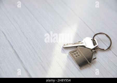 Silberner Schlüssel mit silberner Hausfigur auf weißem Holzhintergrund, Kauf neuer Haus Immobilien Konzept Kopie Raum Stockfoto