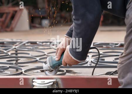 Mann grinst Metallzaun mit Winkelschleifer. Seitenansicht Stockfoto