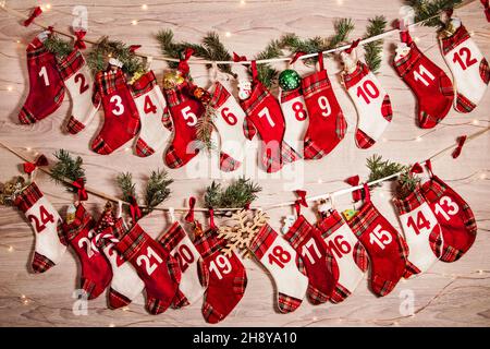 Adventskalender mit Geschenken in Kindersocken, Zweigen eines Weihnachtsbaums, Girlandenlichtern auf einem hölzernen Hintergrund. 24 Socken des Adventskalendes Stockfoto