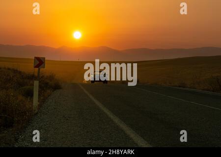 Eskisehir, Türkei - September 12 2021: Altes Auto fährt auf einer Landstraße und der Sonnenuntergang im Hintergrund. Stockfoto