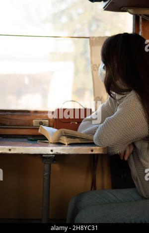 Eine junge Frau in medizinischer Maske reist allein mit dem Zug. Treffen von Vorsichtsmaßnahmen Stockfoto