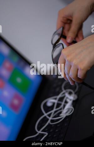 Nahaufnahme der Hände einer Frau, die eine Brille über dem Laptop hält Stockfoto
